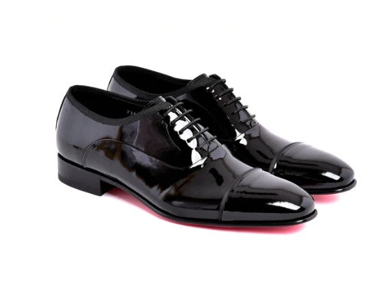 A pair of glossy black patent leather oxford dress shoes with black laces, shown from a three-quarters angle on a white background.