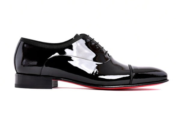 A single black patent leather oxford dress shoe with a cap toe, black laces, and a red sole, shown in profile against a white background.