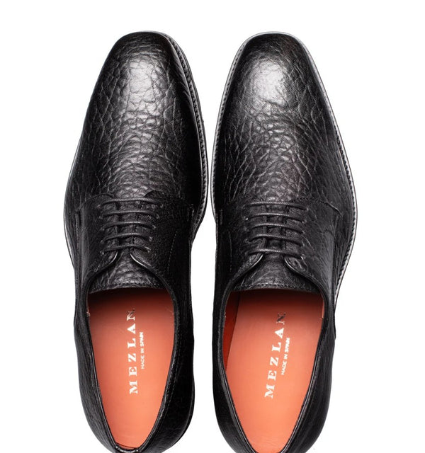 A pair of black textured leather dress shoes with laces, shown from a top-down view on a white background. The orange inner lining features the brand name 'MEZLAN'.