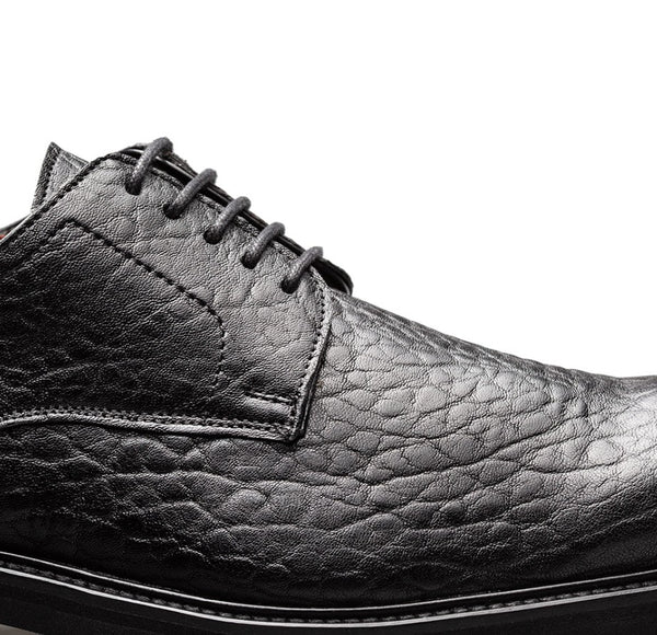 Close-up of a black leather lace-up shoe with a textured, embossed pattern on a plain white background.