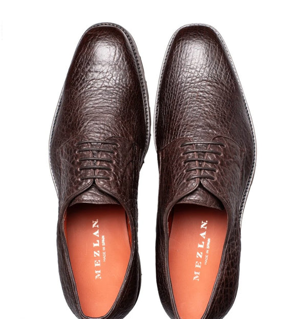 A pair of dark brown textured leather oxford dress shoes shown from a top-down view on a white background, with the Mezlan brand name visible on the orange insoles.