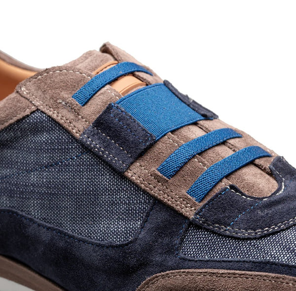 Close-up of a low-top sneaker featuring navy blue denim panels, brown suede overlays, and bright blue elastic laces on a white background.