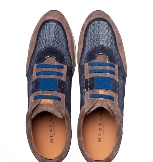A pair of low-top slip-on sneakers shown from a top-down view on a white background. The shoes feature a textured blue denim-like upper, brown suede overlays, and bright blue elastic laces.