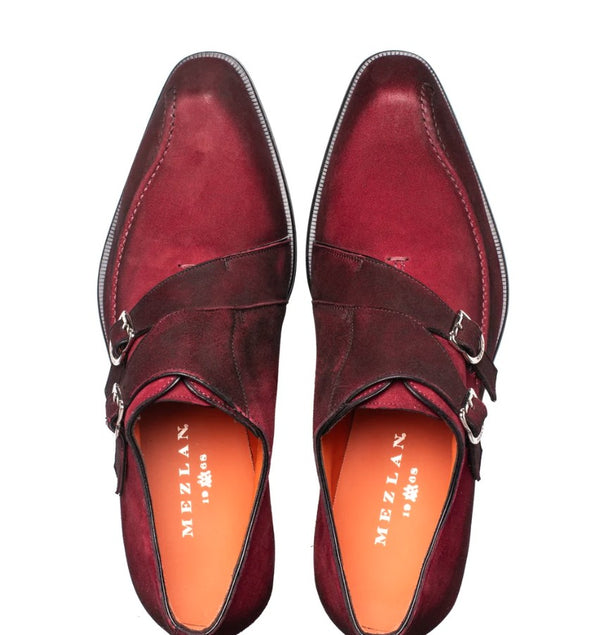 A pair of men's double strap monk shoes in burgundy suede, shown from a top-down view on a white background. The shoes feature silver-tone buckle straps and a contrasting orange insole with the brand name 'MEZLAN' printed in white.