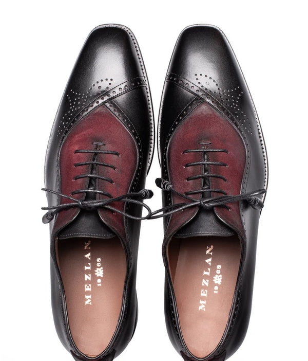A pair of Mezlan men's wingtip oxford shoes shown from a top-down view. The shoes feature a black leather brogue toe and quarter panels with a contrasting dark red suede vamp, black laces, and a tan insole with the Mezlan logo.