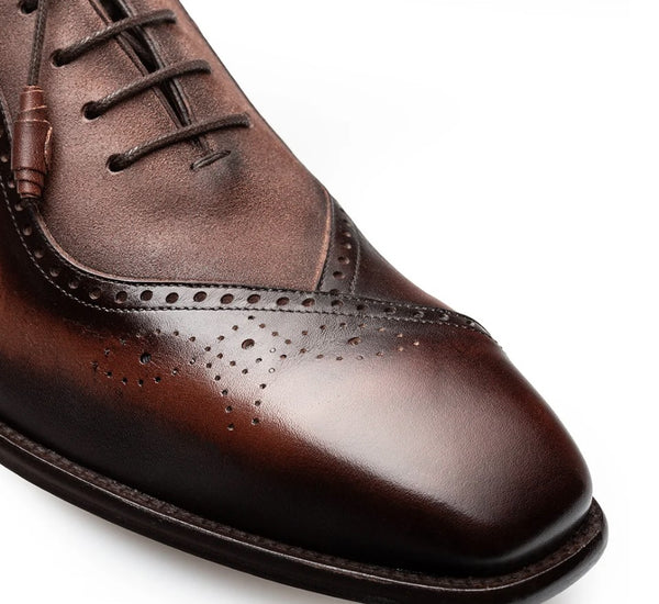 A close-up shot of a men's brown leather oxford shoe, showing the brogue detailing, laces, and polished finish against a white background.