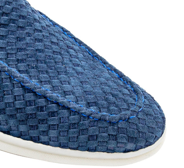 Close-up of a blue woven slip-on shoe showing the textured upper, blue contrast stitching, and a white sole edge against a white background.