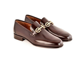 A pair of dark brown leather penny loafers with a silver horsebit detail across the vamp, shown on a plain white background.