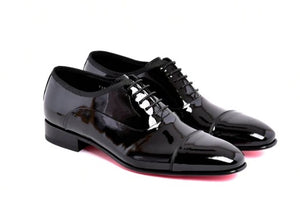 A pair of glossy black patent leather oxford dress shoes with black laces, shown from a three-quarters angle on a white background.