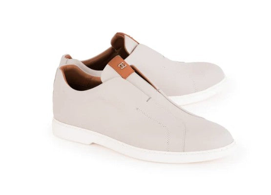 A pair of slip-on casual shoes in light beige with white soles and a small brown leather accent tab on the side, shown against a plain white background.