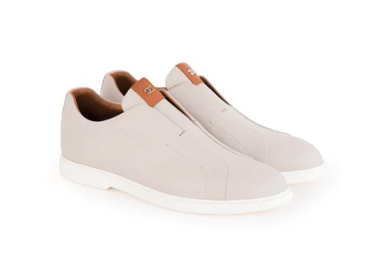 A pair of slip-on casual shoes in light beige leather with a contrasting brown leather pull tab and white soles, shown on a white background.
