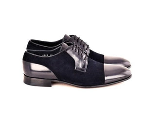 A pair of men's black oxford shoes featuring a mix of smooth black leather and black suede panels, with a glossy black cap toe and black laces, shown against a plain white background.