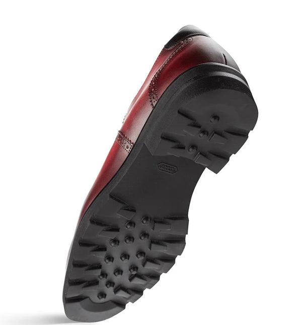 A single red leather shoe shown from the sole side, displaying a black lug sole.