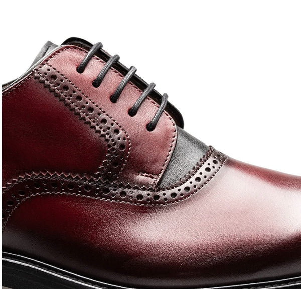 A close-up of a men's oxford shoe in glossy burgundy leather with dark brown brogue perforated detailing and black laces, shown against a plain white background.
