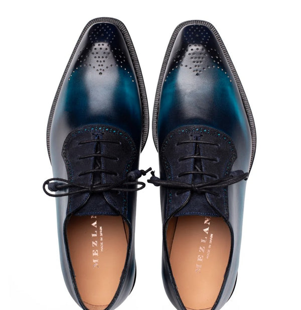 A pair of men's oxford dress shoes with a glossy dark blue and teal gradient finish, featuring brogue detailing on the toe and black laces, shown from a top-down view on a white background.
