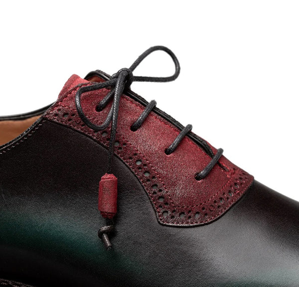 Close-up of a men's lace-up dress shoe with a burgundy suede overlay on the vamp and collar, black laces, and a dangling red cord.