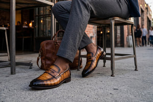 Man sitting at table with brown exotic leather shoes and a briefcase next to him. 