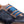 Close-up of a low-top sneaker featuring navy blue denim panels, brown suede overlays, and bright blue elastic laces on a white background.