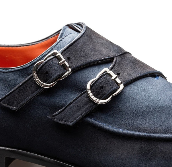 A close-up of a dark navy blue suede double strap shoe with silver buckle closures and a visible orange interior lining.