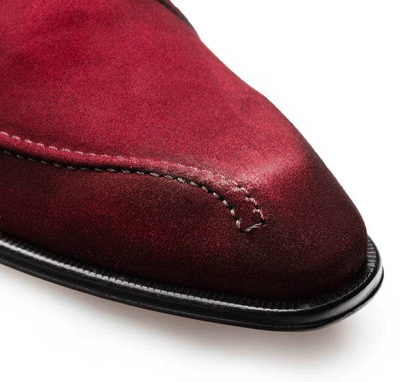 Close-up of a burgundy suede shoe toe with black sole on a white background.