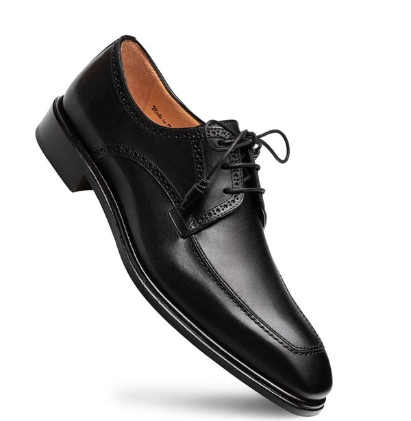 A single black leather dress shoe with a low stacked heel, brogue detailing, and closed lacing, shown on a clean white background.