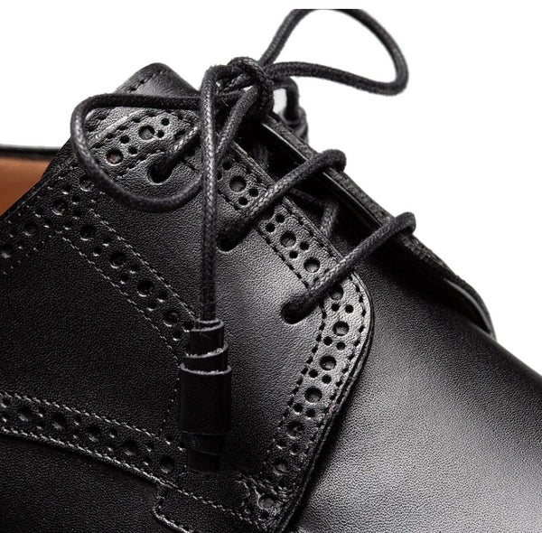 Close-up of a black leather lace-up shoe with brogue perforated detailing and black laces on a white background.