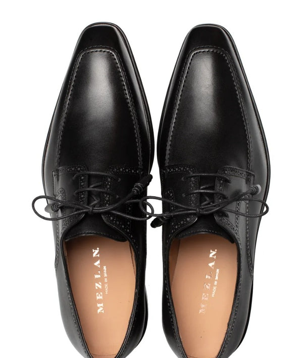A pair of black leather dress shoes with pointed toes and black laces, shown from a top-down view on a white background. The insole is tan with the brand name 'MEZLAN' printed in gold.
