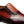 A close-up of a men's slip-on dress shoe in rich brown leather with a gradient finish, featuring decorative brogue perforations and a textured upper panel.