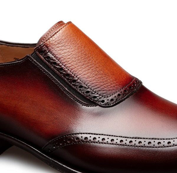 A close-up of a men's slip-on dress shoe in rich brown leather with a gradient finish, featuring decorative brogue perforations and a textured upper panel.