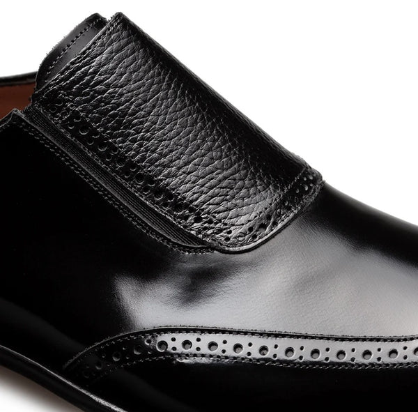 Close-up of a black leather slip-on dress shoe with brogue detailing on a white background.