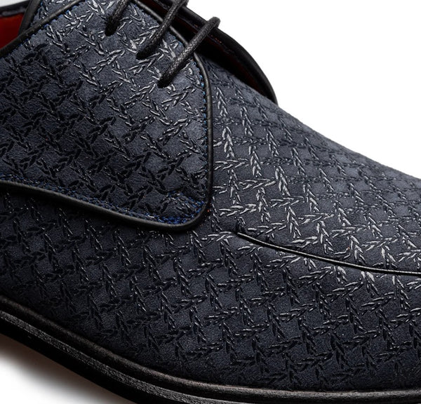 Close-up of a dark navy blue leather shoe with an embossed geometric pattern and black laces, shown on a white background.