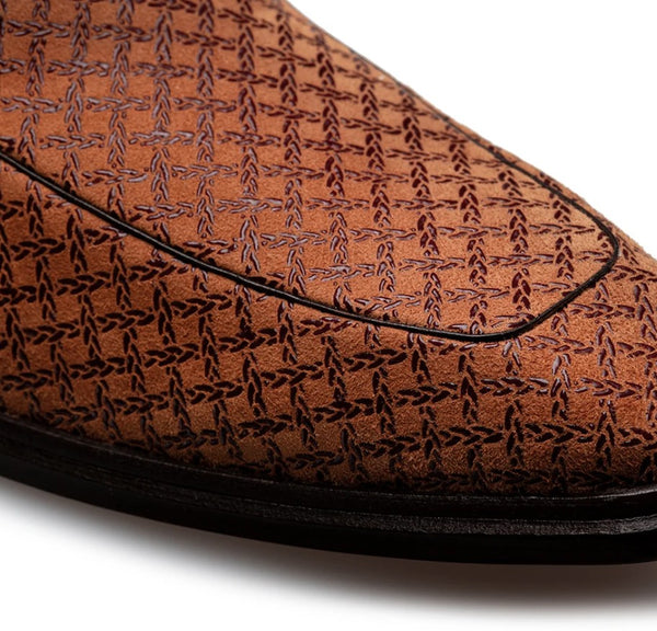 Close-up of a brown textured loafer with an embossed geometric pattern and black piping along the vamp, shown on a white background.
