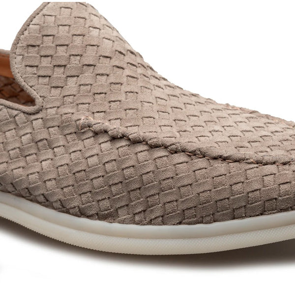 A close-up of a woven slip-on loafer in taupe suede with a white sole, shown against a plain white background.